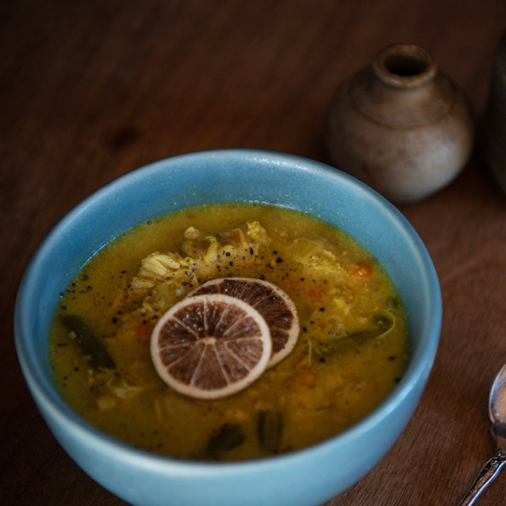 A bowl of Thai yellow chicken curry with coconut milk, garnished with a slice of lemon, served on a dark wooden table.