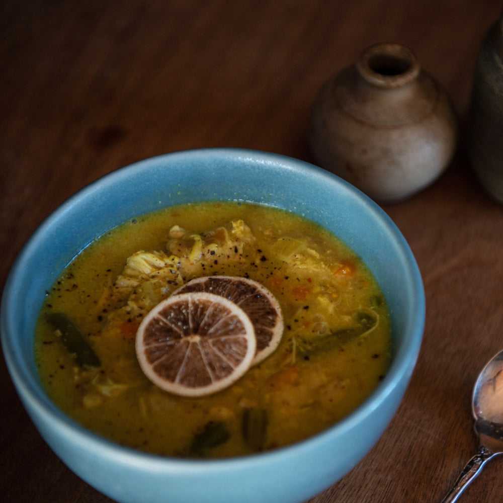 A bowl of Thai yellow chicken curry with steamed rice and greens, garnished with a slice of lemon.