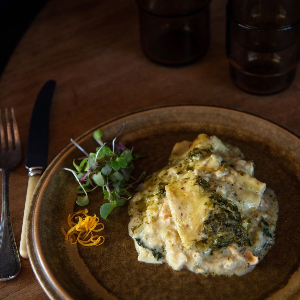 A plate of seafood lasagne served with a side of green salad and lemon zest garnish.